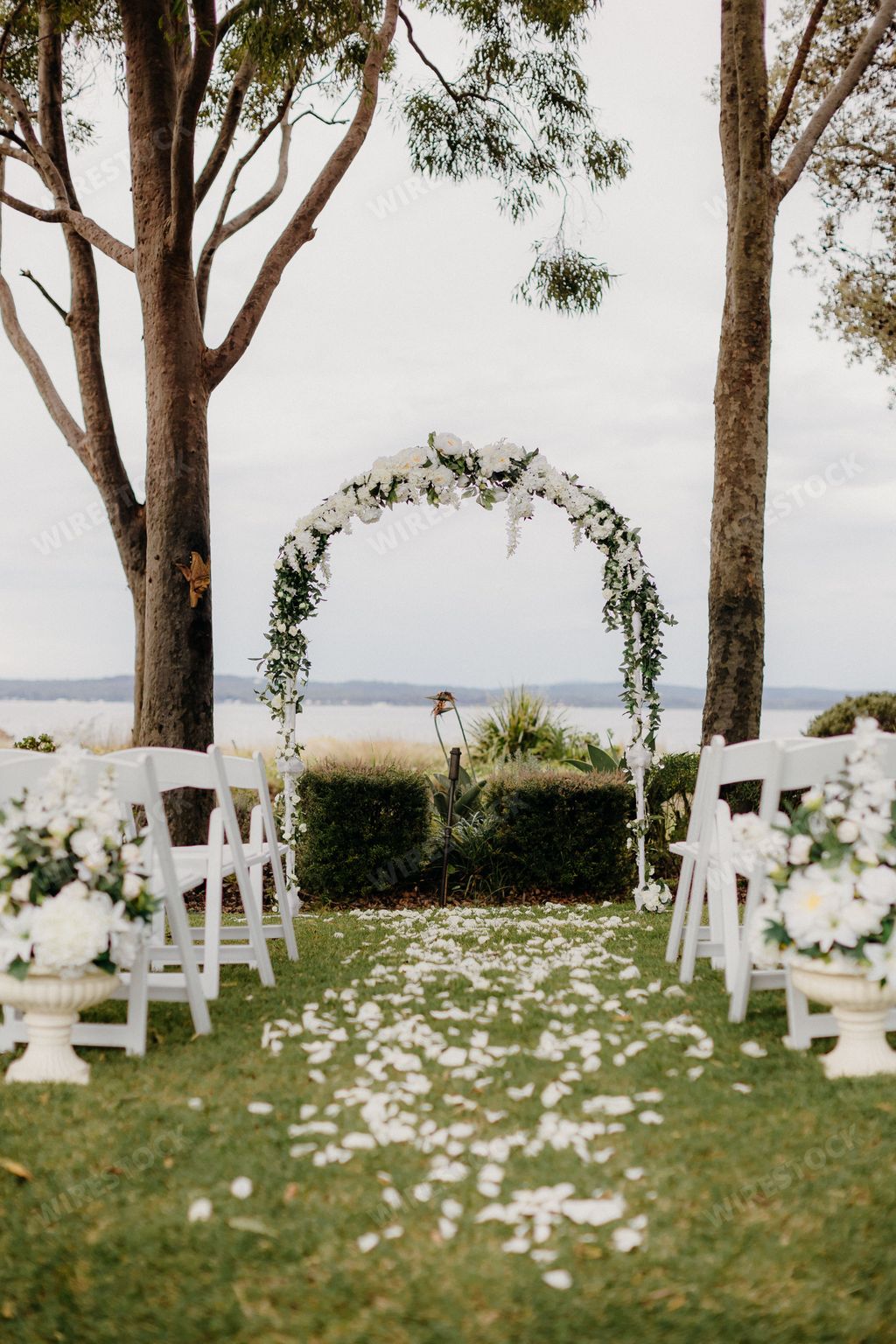 AN outdoor wedding ceremony setup with white floral arch and chairs