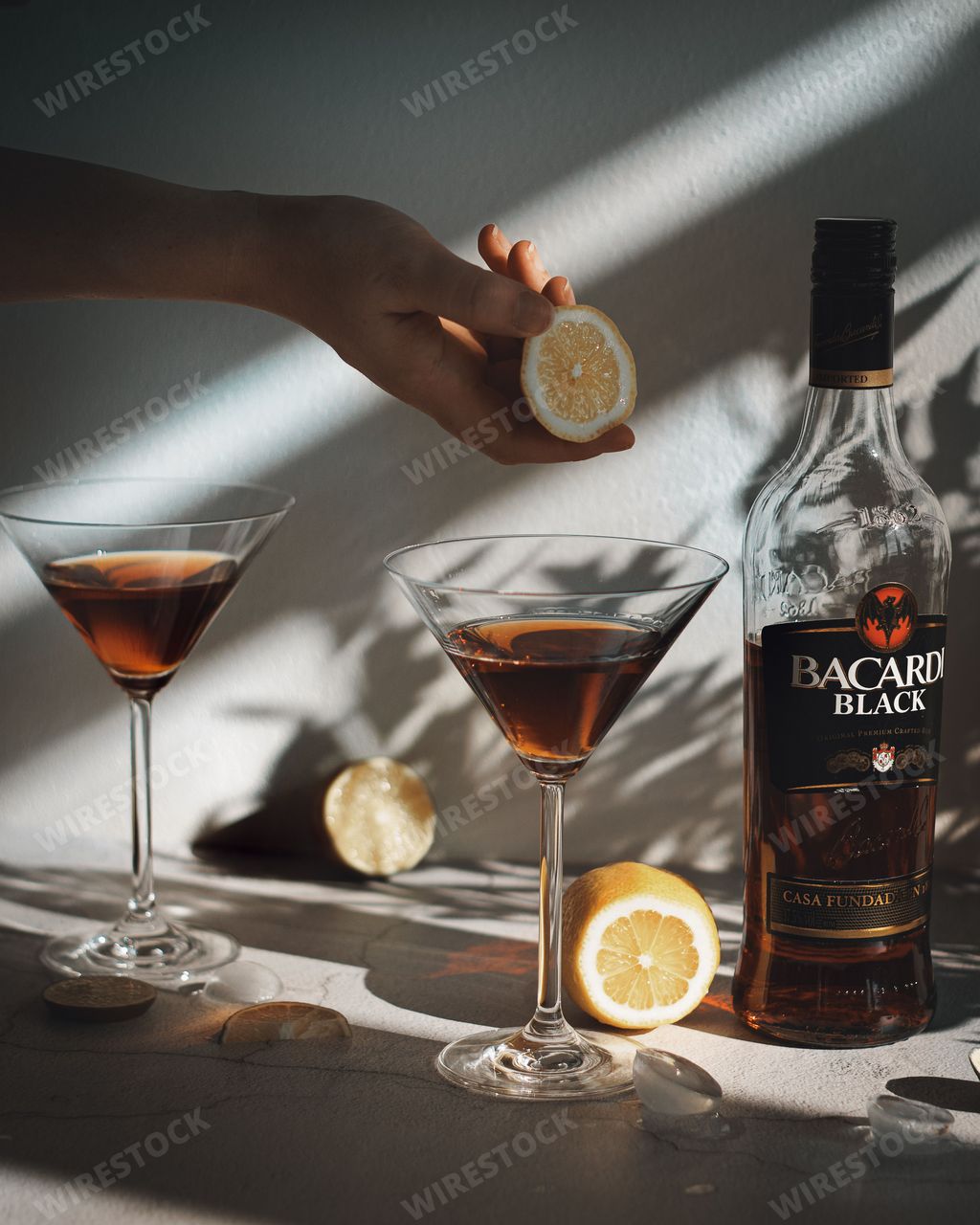 A beautiful vertical view of a hand squeezing lemon juice on a Bacardi-based cocktail on a summer day