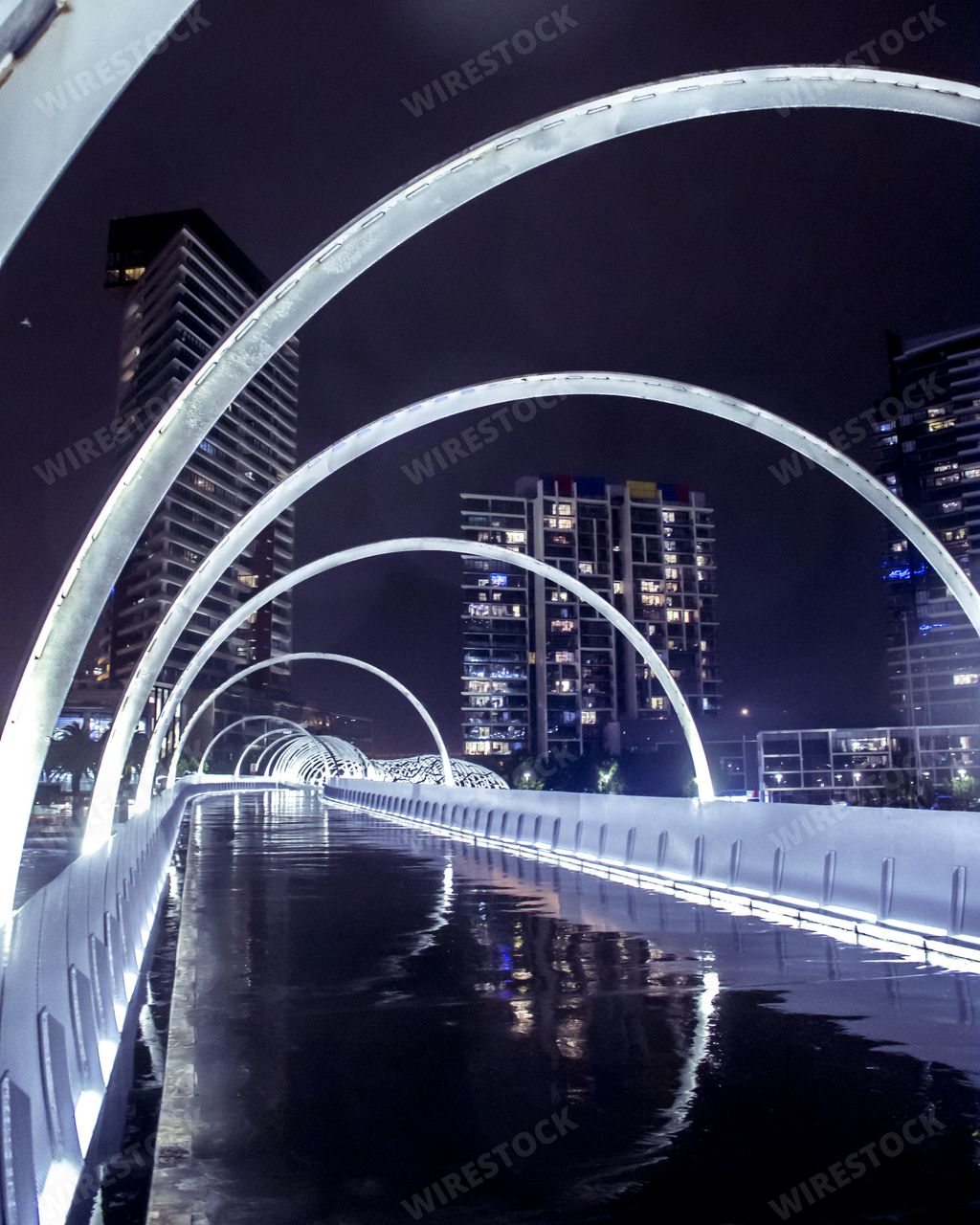 A water bridge with metal arches flowing through an urban city with skyscrapers in the background