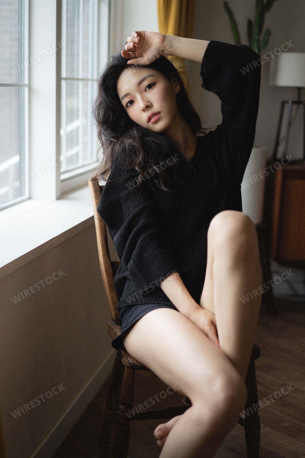 A vertical shot of a beautiful young South Korean female sitting on a wooden chair
