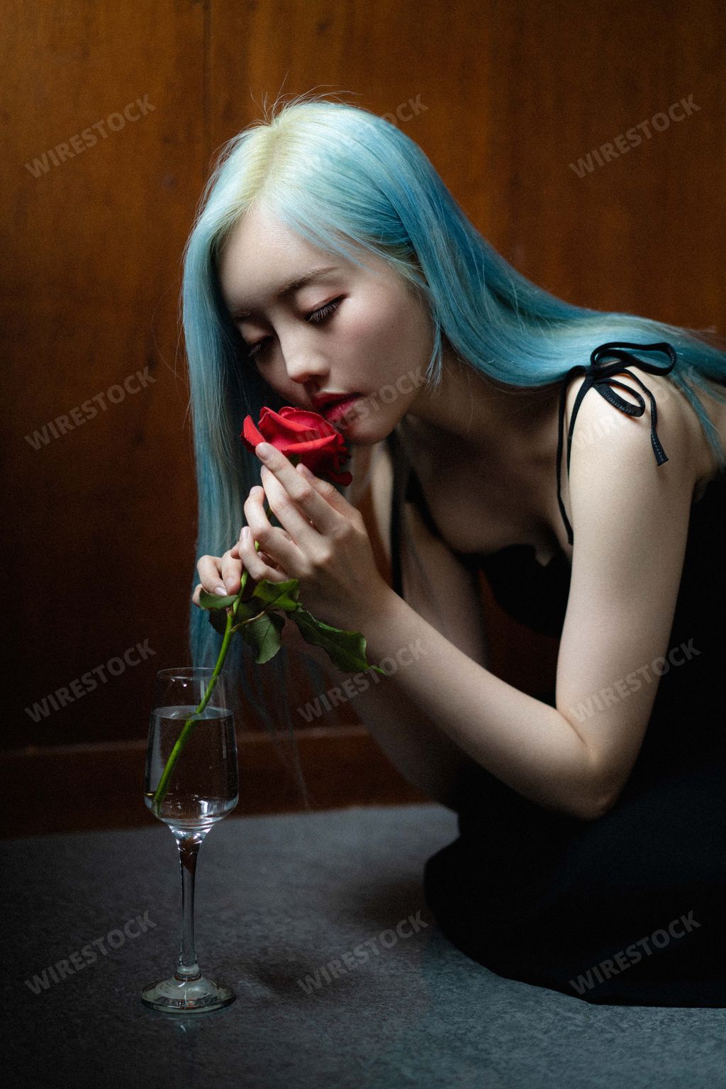A young blue-haired South Korean female putting a single red rose in a wine glass