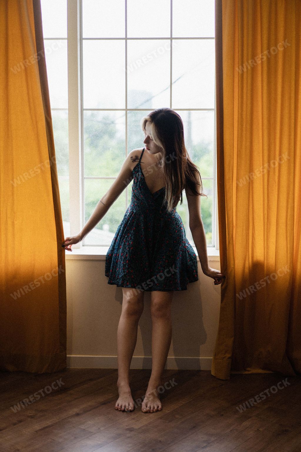 An adult Korean woman wearing a dark blue floral dress and sitting on a windowsill