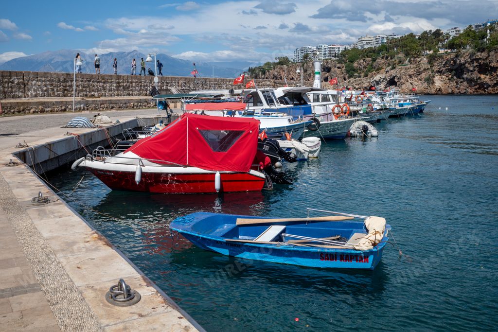 Scenic view of a marina with colorful boats docked along the pier and people walking on the promenade in Antalya, Turkey
