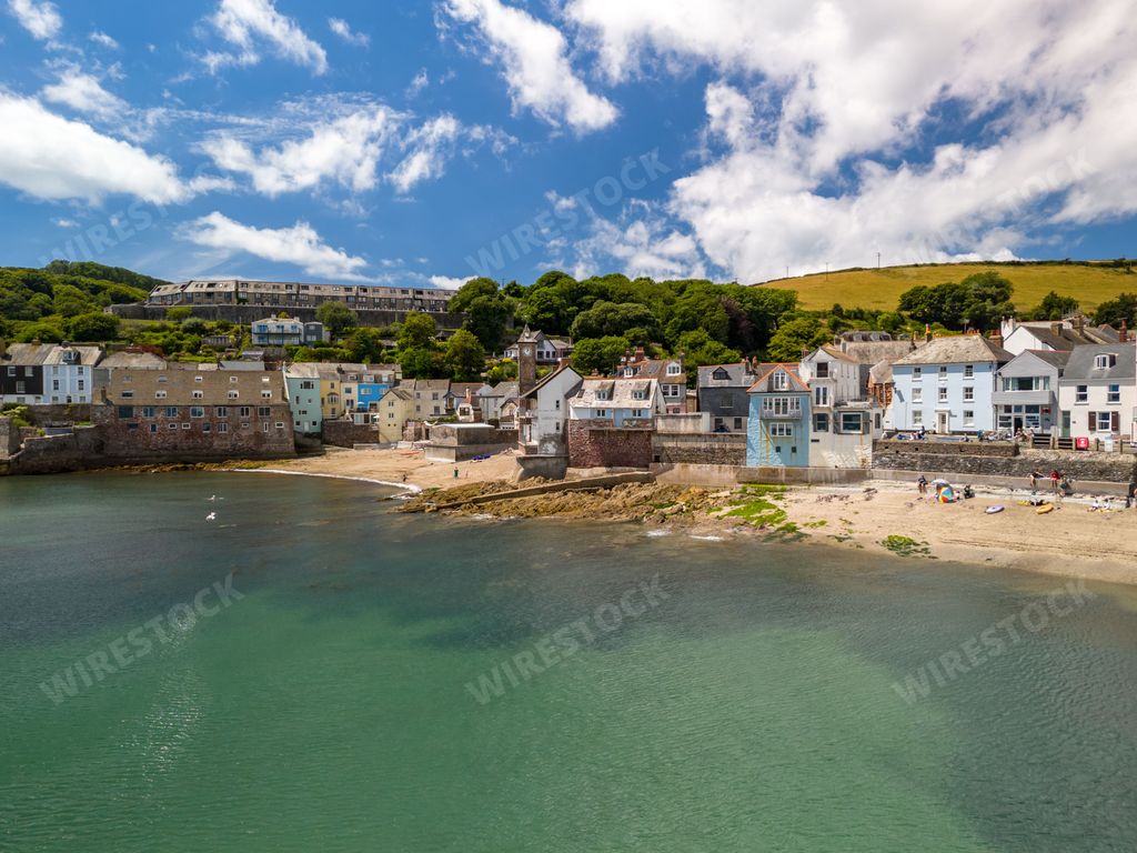 A picturesque coastal village with colorful houses along the shoreline under a clear blue sky in Cornwall, England