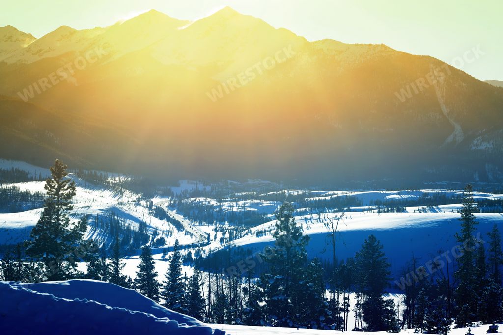 A beautiful view of the sun shining over the mountain and the snow-covered hills