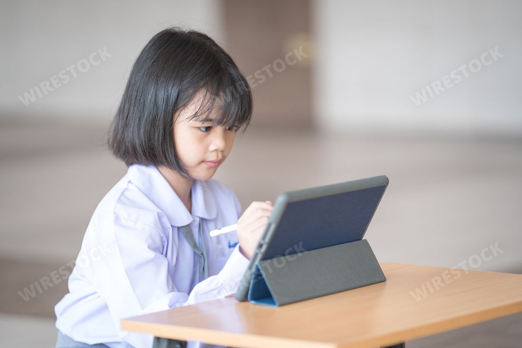 A Southeast Asian school girl in a uniform with short black hair drawing on a tablet with a pen