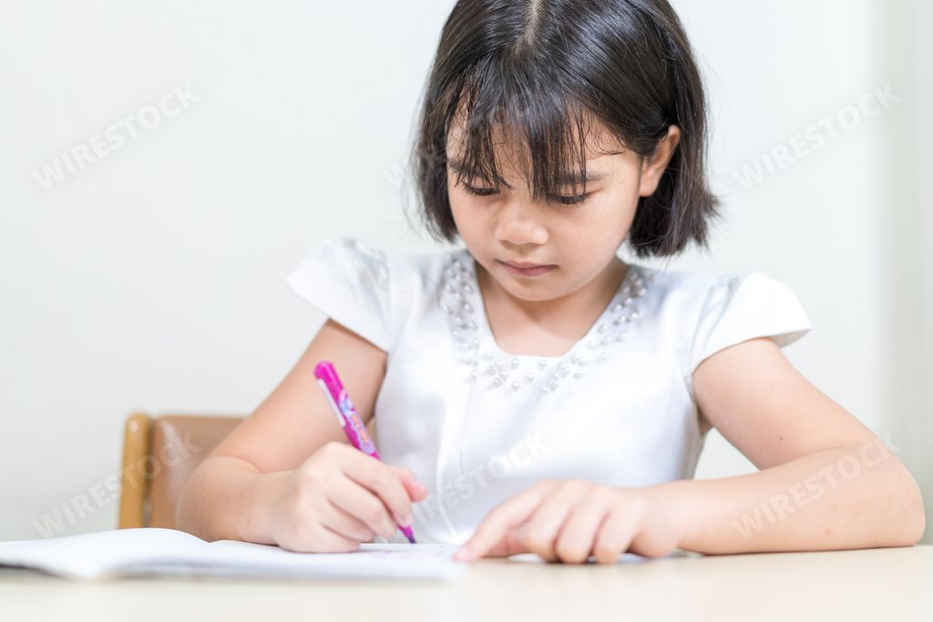 An asian little girl sitting by a desk and writing in her copybook