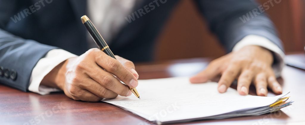 A close-up shot of male hands holding a pen over paper documents.