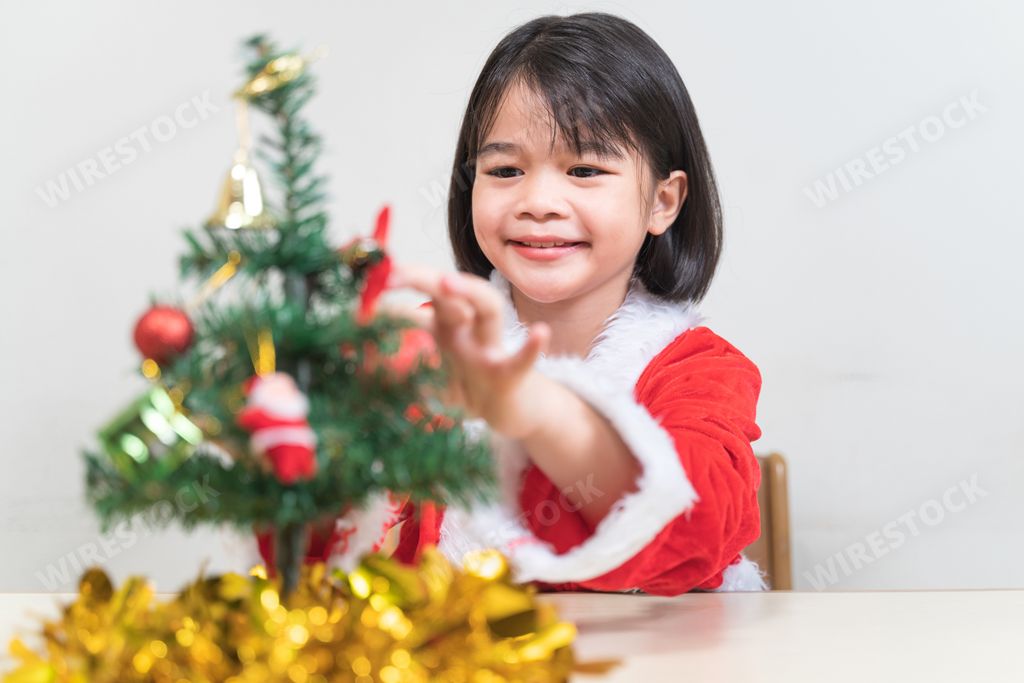 A view of cheerful Asian female kid wearing Santa Claus clothes and decorating the Christmas tree