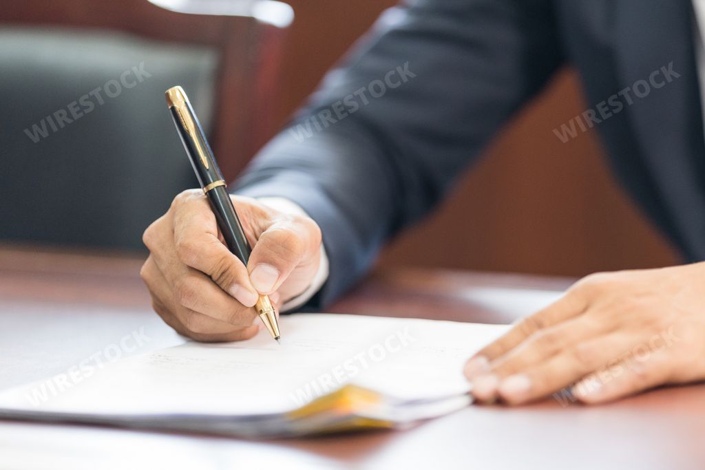 A close-up shot of male hands holding a pen over paper documents.
