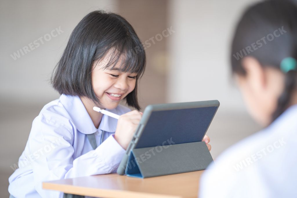 A happy smiling cute Southeast Asian school girl in a uniform drawing on a tablet with a pen