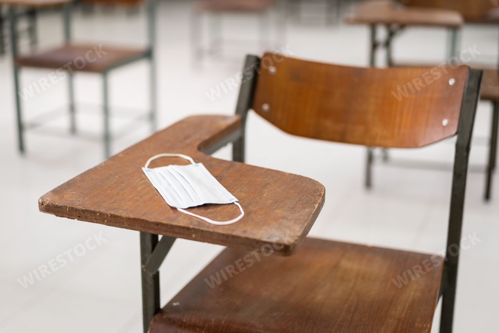 A used medical facemask on a wooden chair in an empty classroom during COVID-19 pandemic