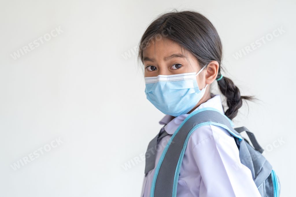 A cute beautiful Southeast Asian school girl with braids in a uniform wearing a mask due to the pandemic