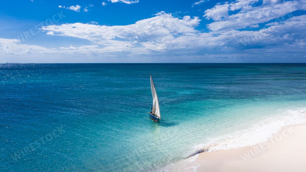 An aerial shot of a sailboat in the calm blue ocean with the horizon and the sky in the background