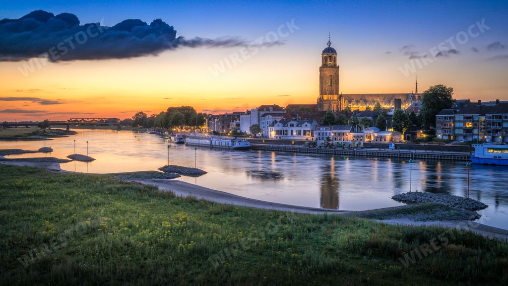 A stunning landscape image of a riverbank at sunset, with the sun's rays reflecting off the water