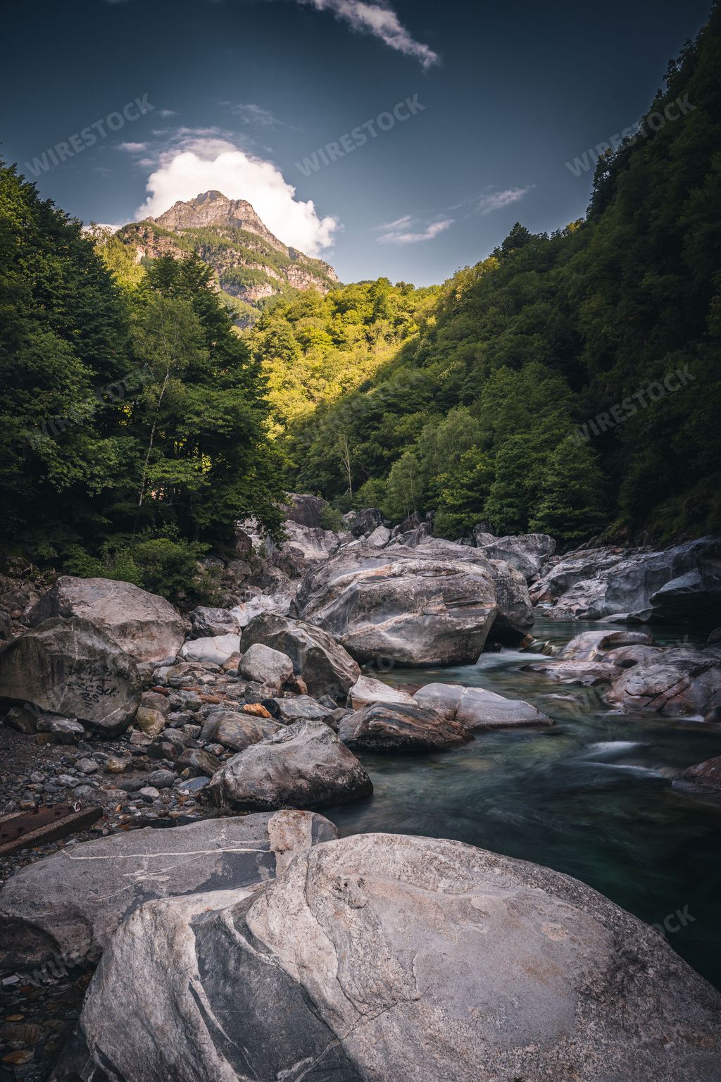 A vertical shot of Water flowing between stones with mountains in the background, Lavertezzo, Switzerland, Canton Ticino