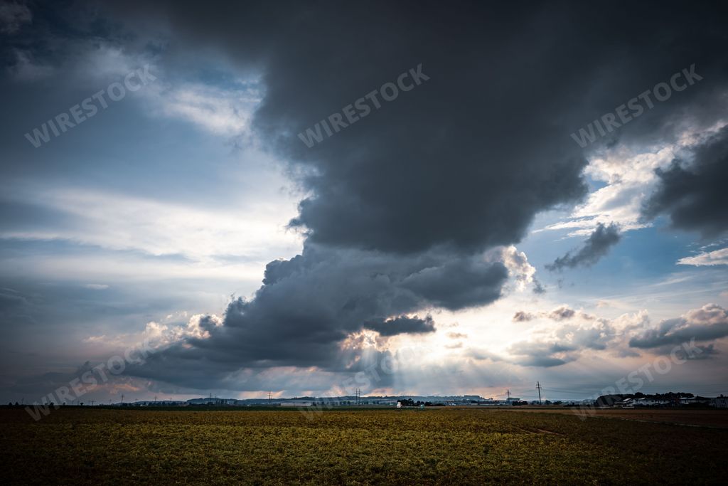 A field surrounded by dramatic clouds before the storm with a forest in the background