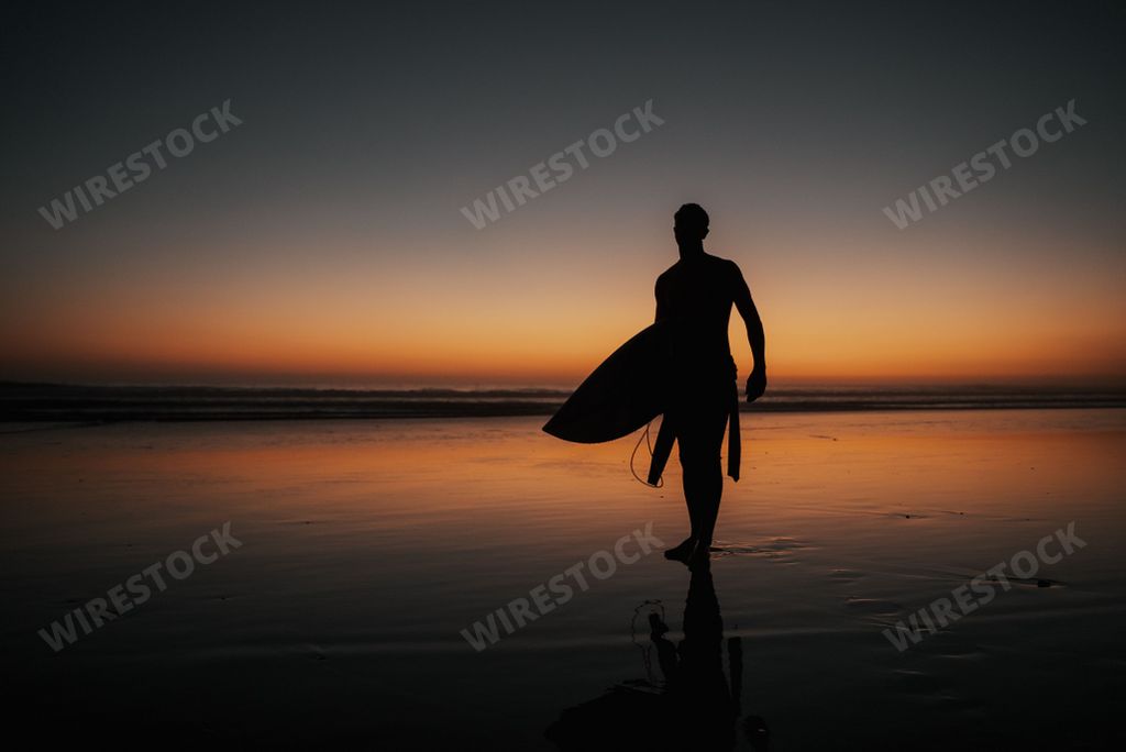 A person with a surfing board walking on the beach at sunset perfect for wallpapers and backgrounds