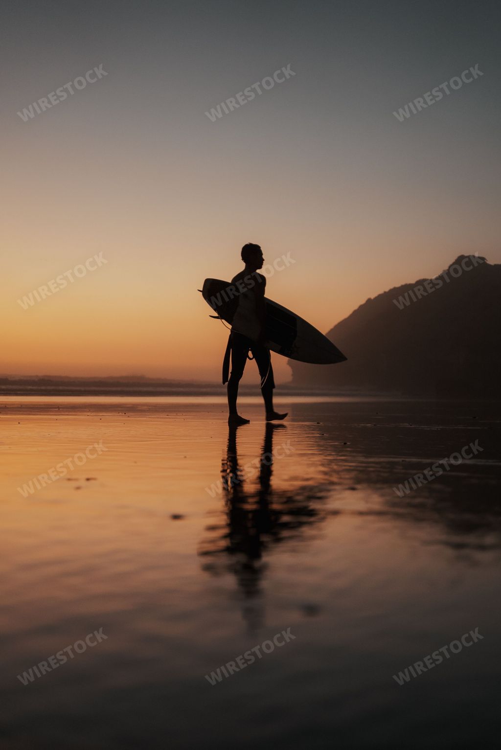 A vertical shot of a person with a surfing board walking on the beach at sunset perfect for wallpapers