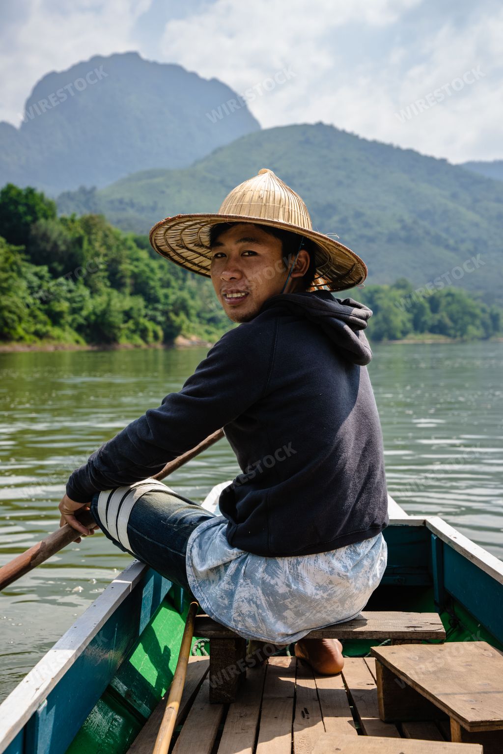 The Asian boy with a straw hat on the riverboat  on the Nam Ou River in the Mountains of Nong Khiaw, Laos, vertical