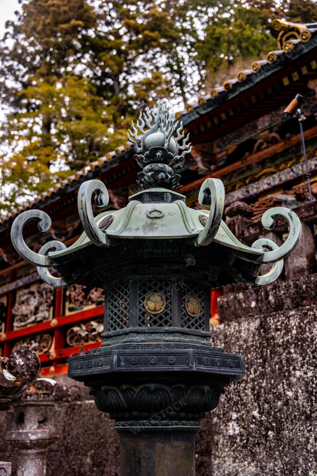Vertical shot of ornate ancient Japanese metal lantern with ornate stone wall in the background at Nikko Toshogu shrine in Nikko Japan.