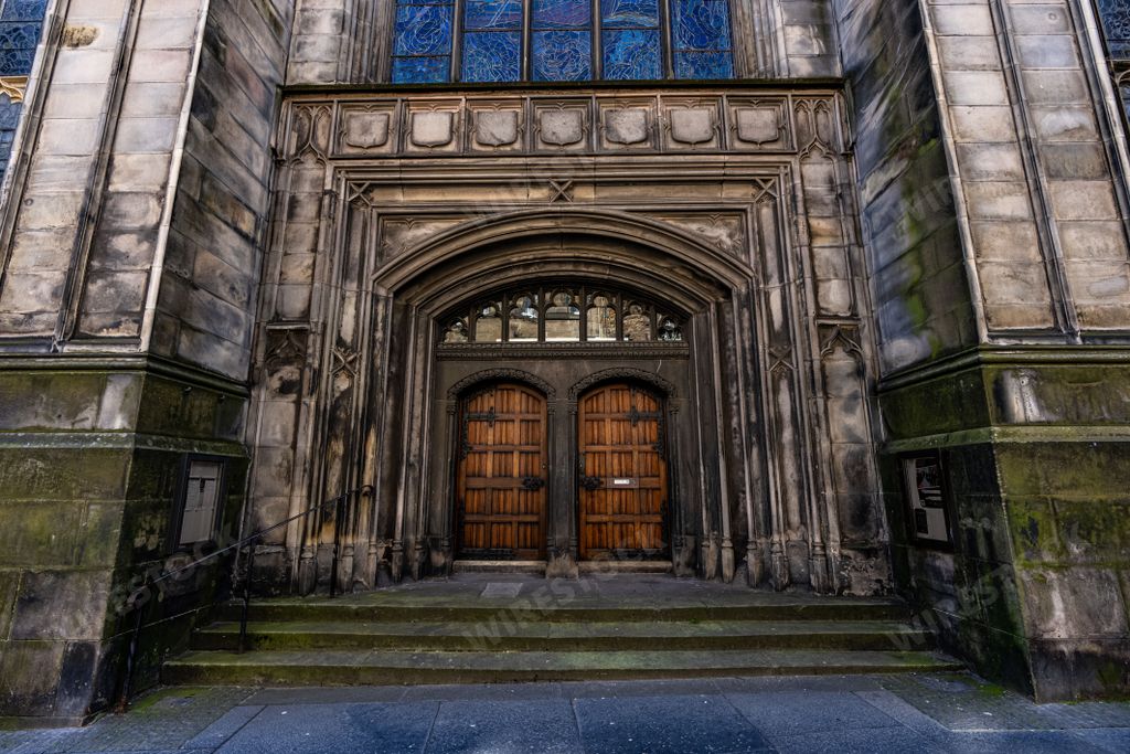 An ancient stone cathedral with double wood doors surrounded by stone and stained glass windows