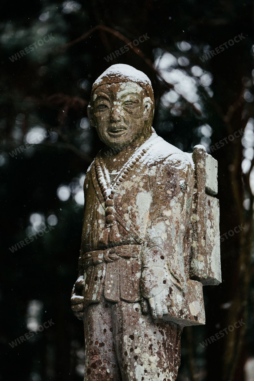 Snow and moss-covered Japanese traditional stone lantern with forest at the Fujiyoshida Sengen Shrine.