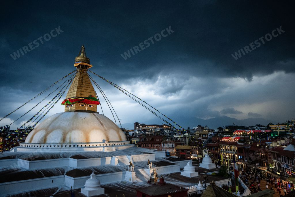 An aerial view of Boudhanath Stupa temple dome with prayer flags under dark cloudy stormy sky