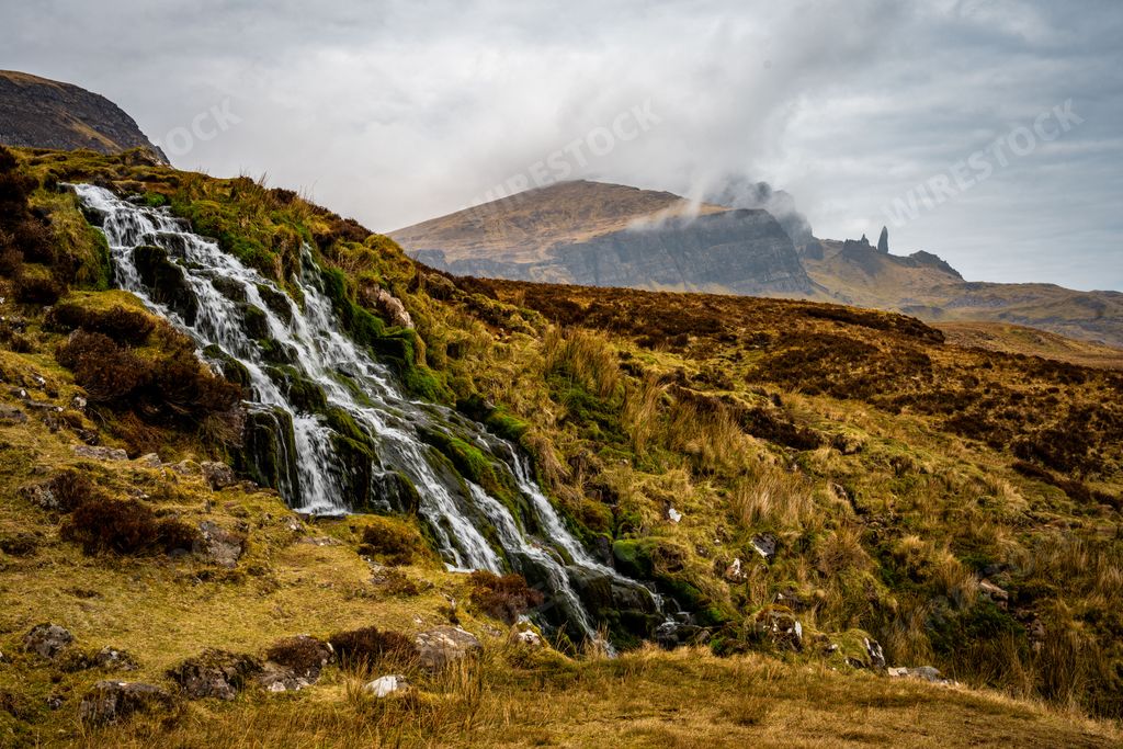 A beautiful waterfall flowing down the rocks covered in moss with foggy mountains in the distance