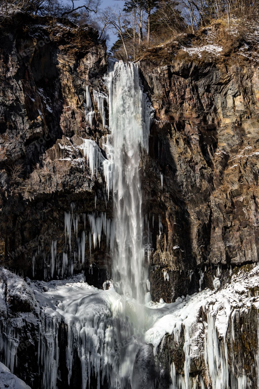 Stunning vertical shot of half-frozen Kegon Falls with snow, icicles and icy streams in the foreground