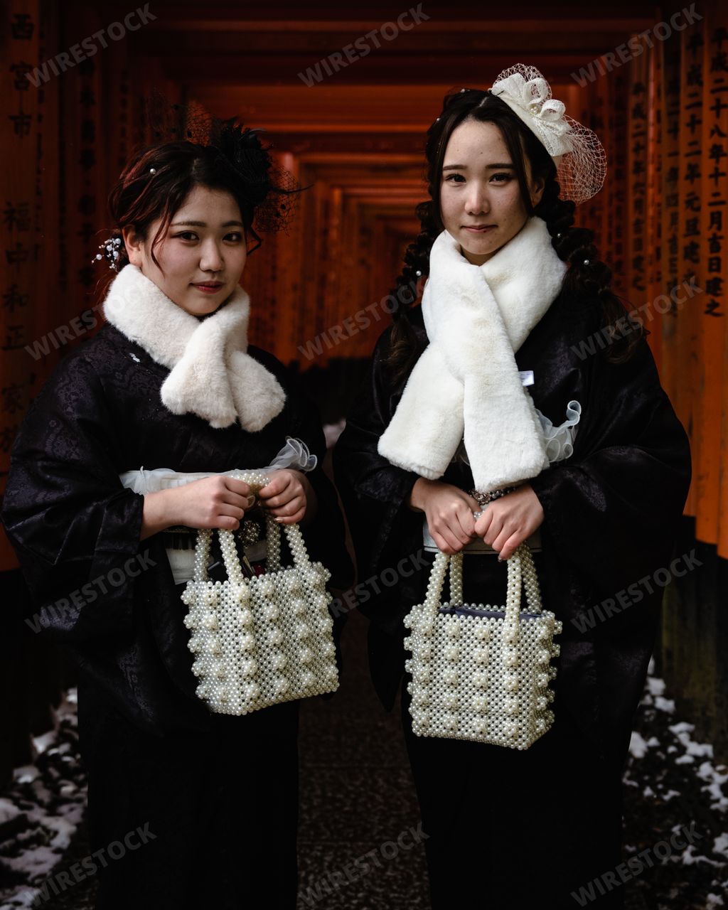 Two Young Japanese Women in formal winter attire posing in front of the Torii Gate Tunnel at Fushimi Inari Shrine in Kyoto Japan.