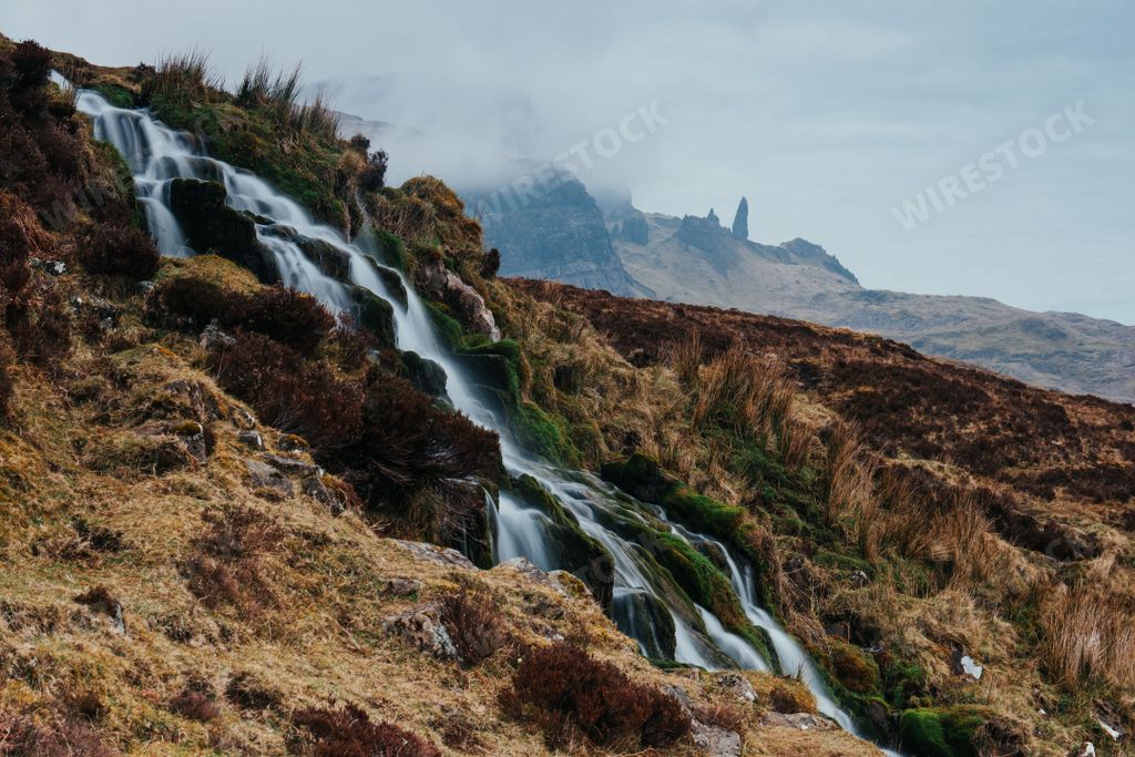 A beautiful waterfall flowing down the rocks covered in moss with foggy mountains in the distance