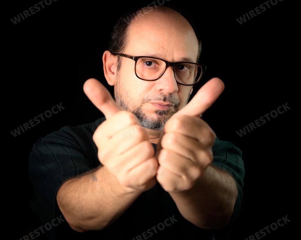 A closeup of a bearded man wearing glasses and gesturing with his hands against a black background