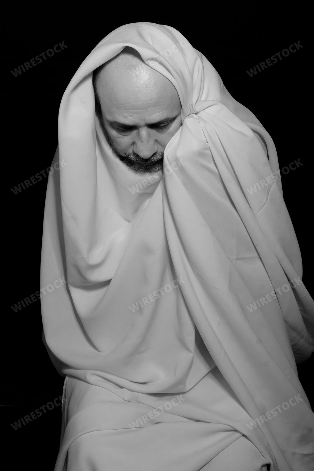 A Brazilian man covering his face with a white cloth against a black background