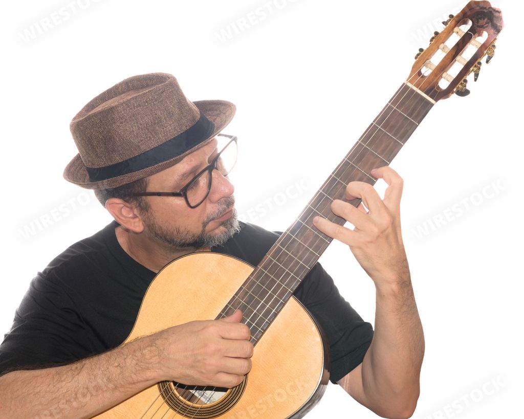 A White bearded man from Brazil wearing eyeglasses and a hat playing the guitar