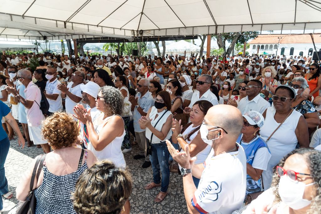 A diverse group of people gathered together in front of a white canvas tent, one person in the center of the crowd holding a microphone