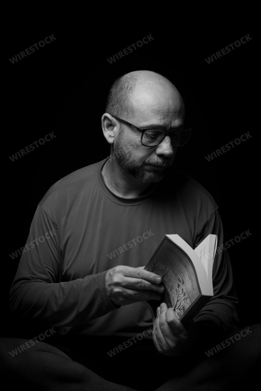 A portrait of a bearded, bald man reading a book against a black background in Salvador, Bahia, Brazil