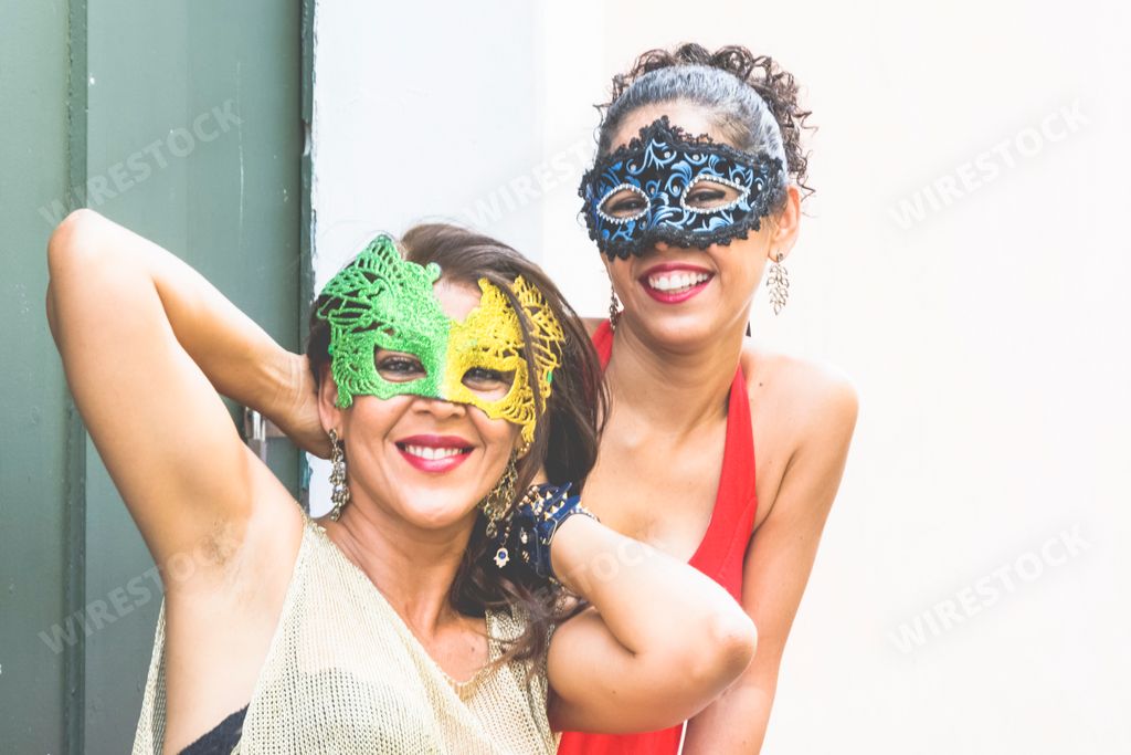 A close-up shot of two women wearing masquerade masks posing in front of the camera in one of the streets of Brazil
