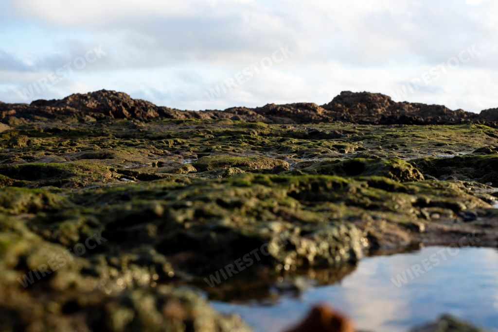 Beach rocks totally wet with water in the form of a puddle making reflections of the blue sky in a day of strong and bright sun.