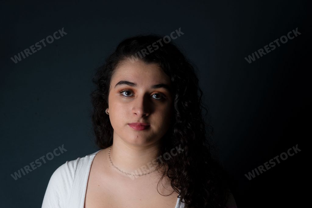 A young woman with a stoic expression stares directly at the camera