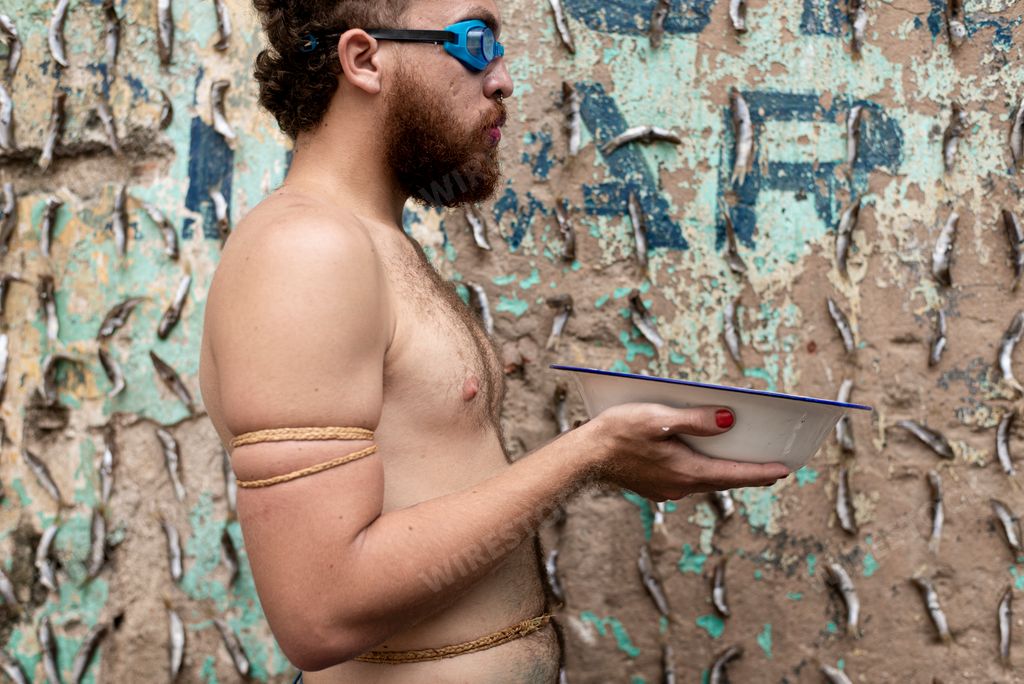 A closeup portrait of a Man performing a protest performance with a bowl of water against a wall