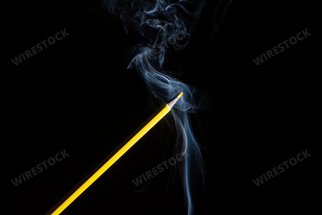 A yellow colored pencil touching the white smoke coming from below. Close up. Sharp pencil scraps.