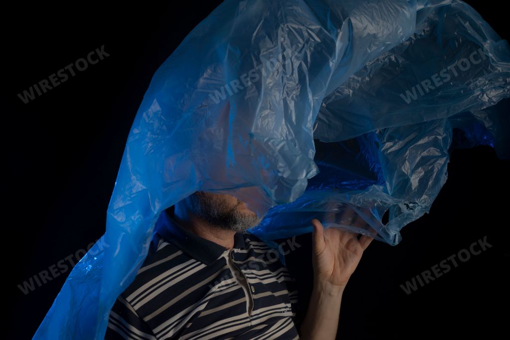A sad bald mature man suffocating with a plastic bag flying over his head full of thoughts