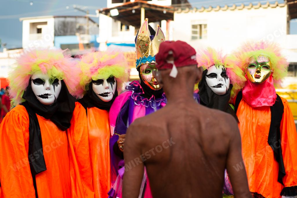 A shirtless man in front of a group of people dressed for a carnival, Brazil