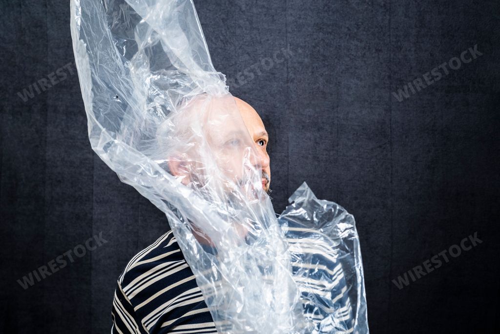 A Mature man suffocating with transparent plastic bag flying over his head