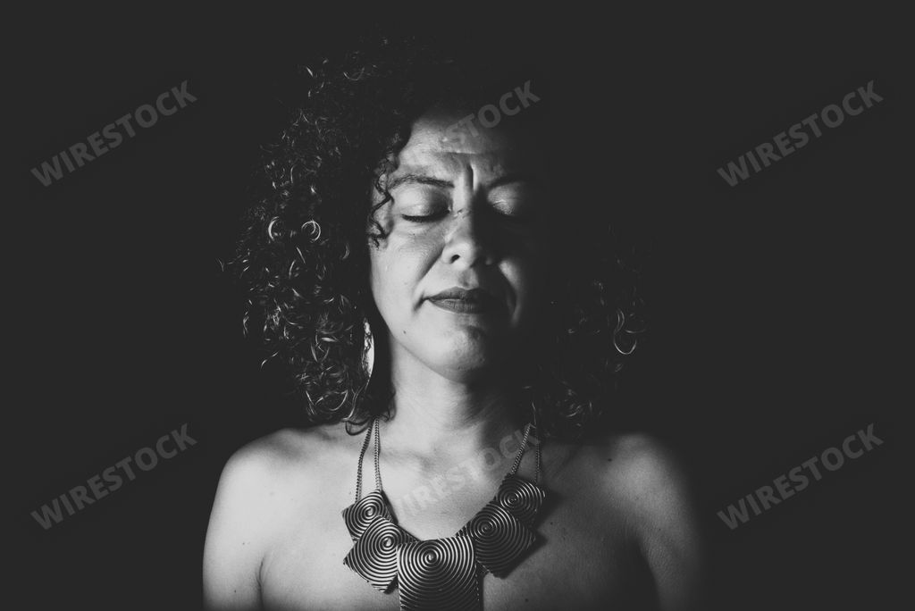 Afro-Brazilian model in portrait with eyes closed photographed in studio with black background. Concept of awareness, maturity and femininity.
