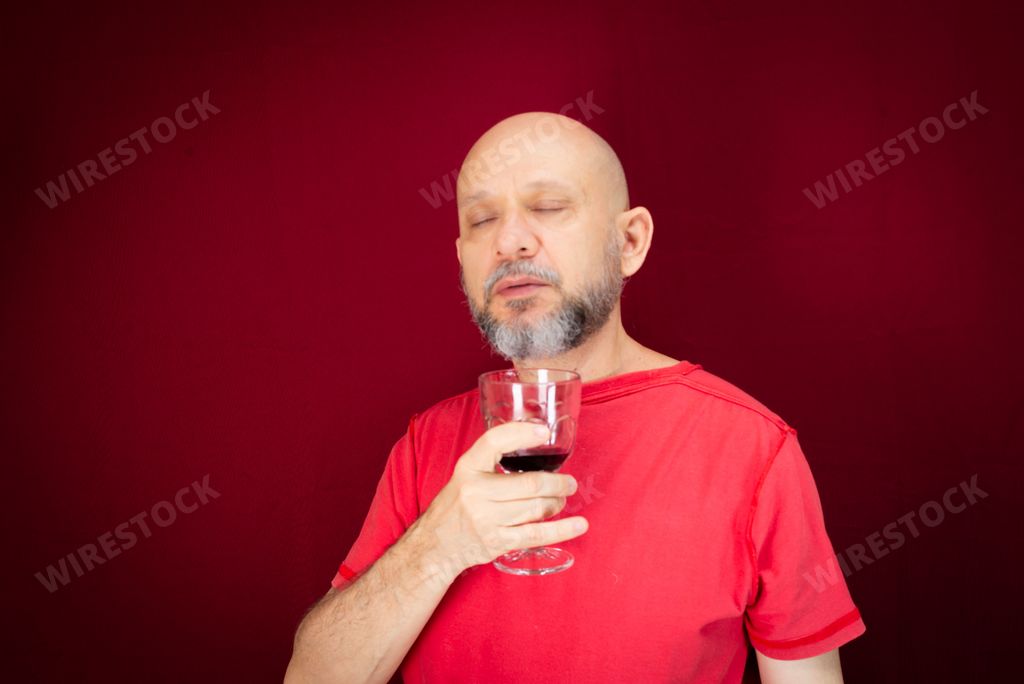 A man holding a glass of wine while standing over a red background