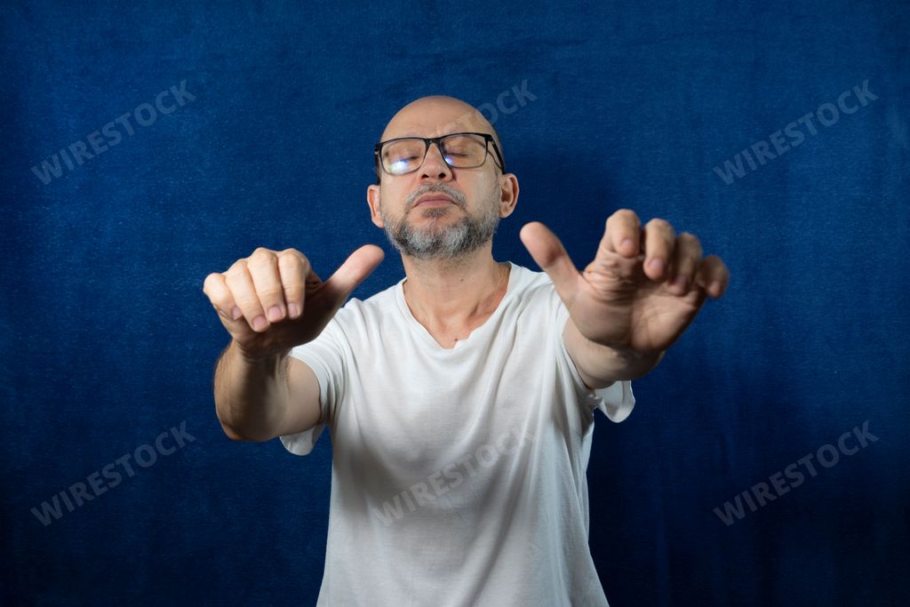 The portrait of a bearded bald man imitating something with his hands against the blue background