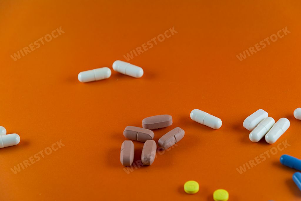 Different pills of brown white blue and yellow color scattered on orange color background. Medical supplies.