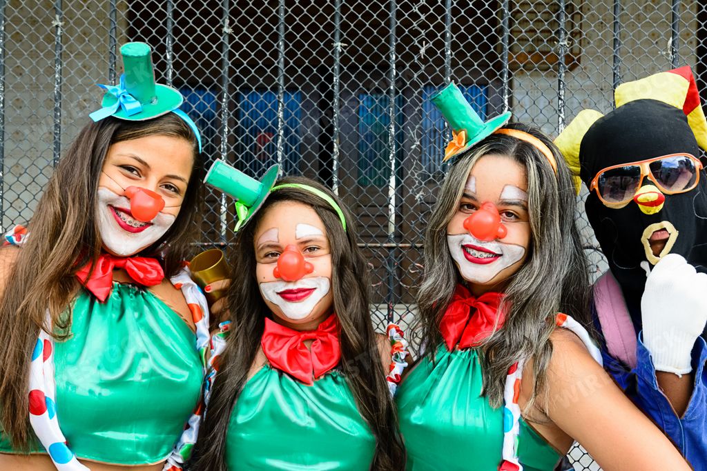 Three female models wearing clown hats and colorful face paint, smiling and posing together against a white background